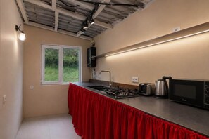 Cuina compacta amb fogó a gas, microones i bullidor d'aigua. Hi ha una finestra que ofereix vistes a la vegetació.