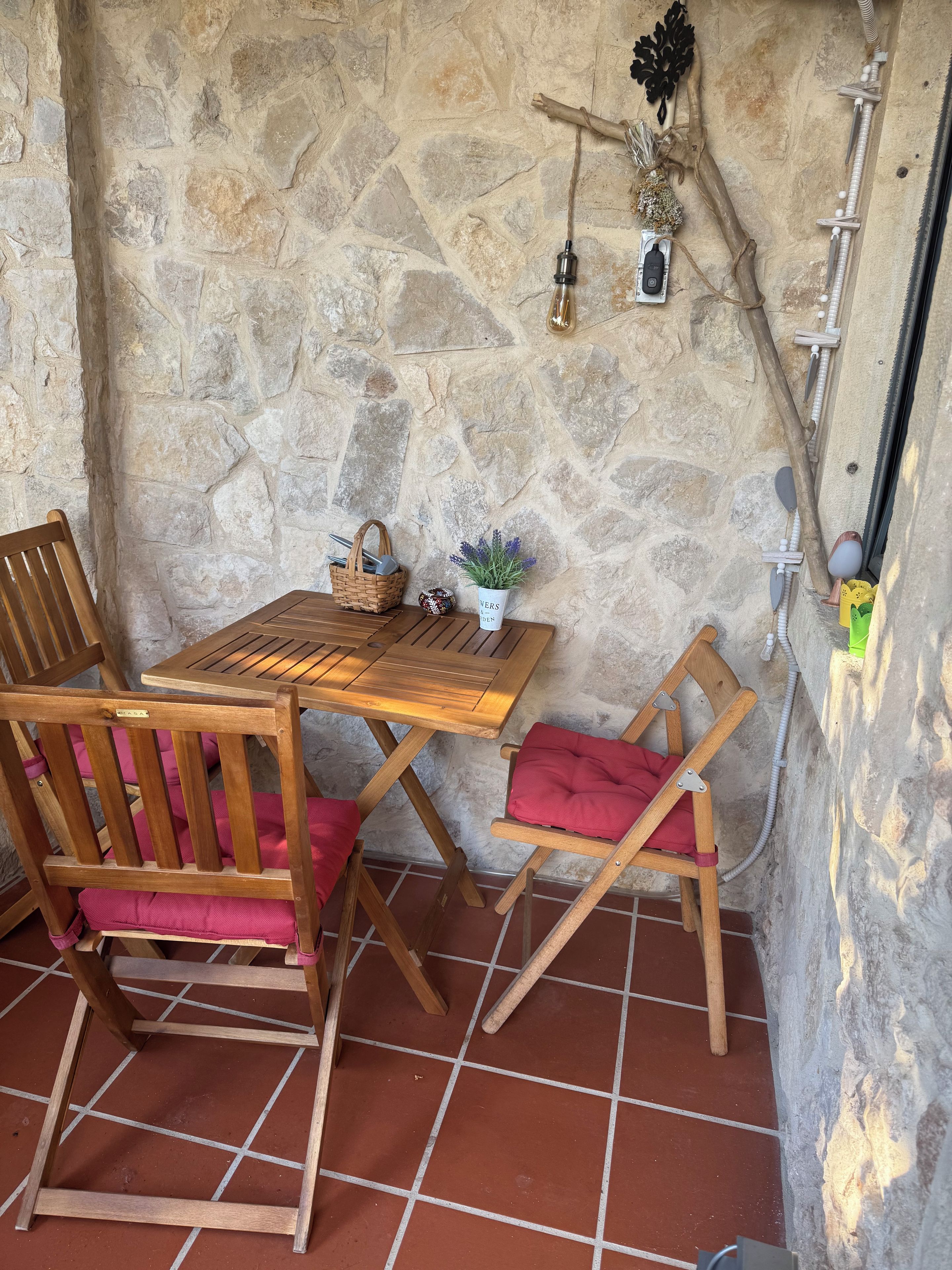 Un muro de piedra con una mesa y sillas de madera, una pequeña planta en maceta y un adorno.
