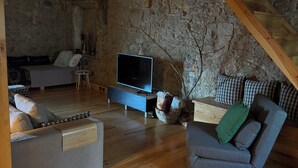 A rustic room with a stone wall, wooden beams, a sofa, a chair, and a television.