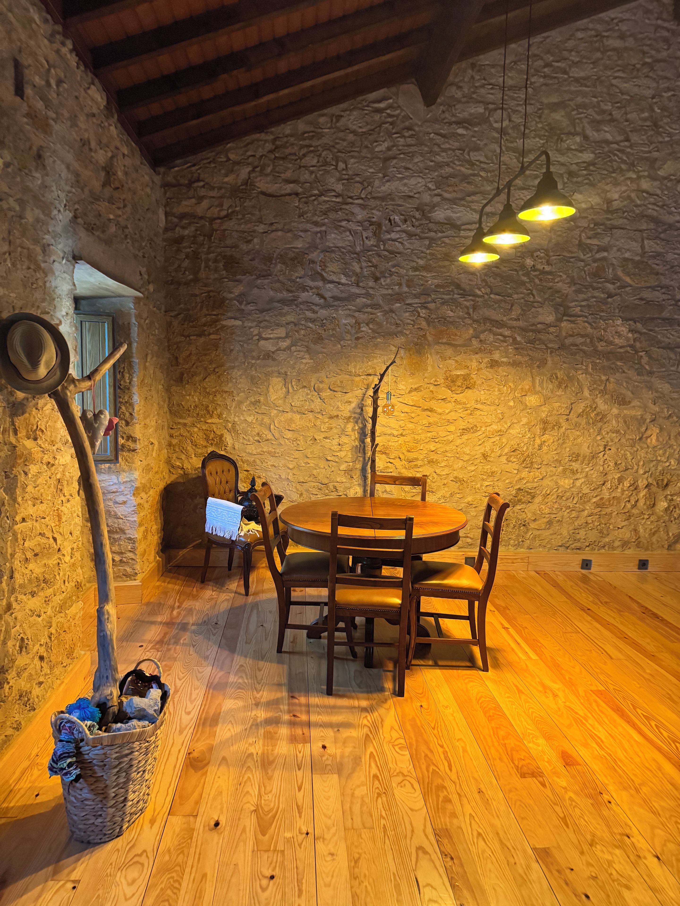 A rustic dining area with a stone wall, wooden floor, and a round table with chairs.
