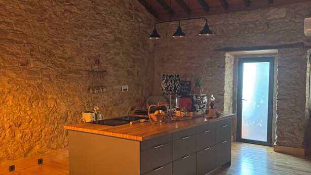 A kitchen with a stone wall, wooden ceiling beams, and a large island with drawers.
