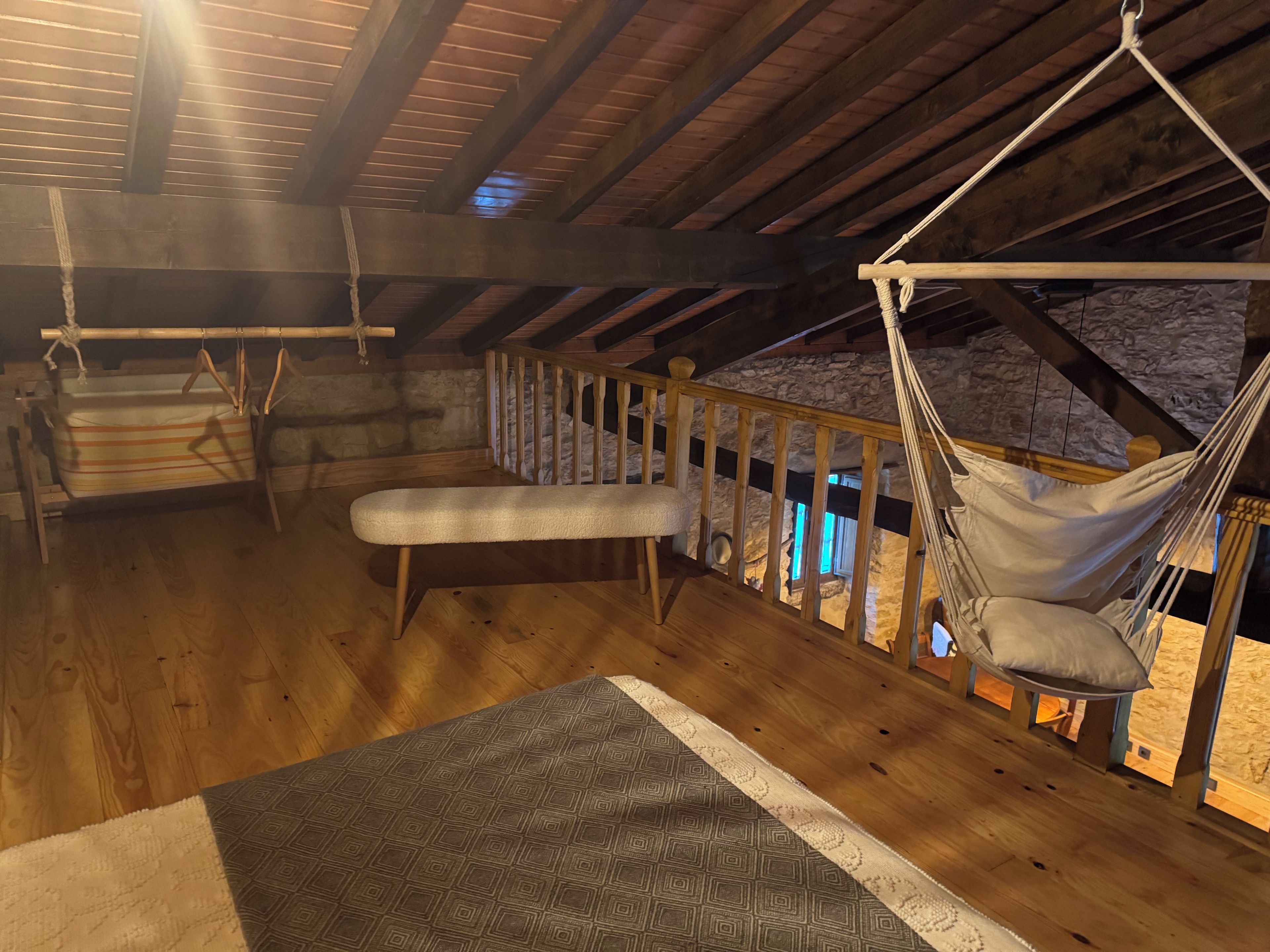 Eine Holzterrasse mit einer Hängematte, einer Bank und einem Hängekorbsessel.
