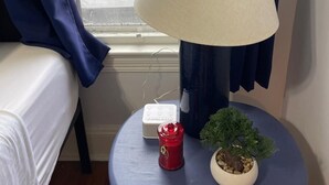 Ett rum med en säng, en lampa på ett litet bord, ett rött ljus och en liten krukväxt.
