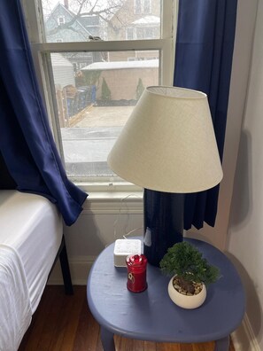 Een kamer met een bed, een lamp op een tafeltje, een rode kaars en een kleine kamerplant.