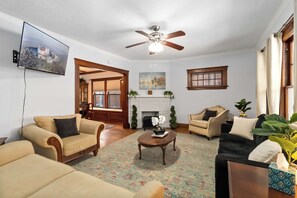 A living room with a fireplace, a ceiling fan, and a television mounted on the wall.