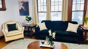 A living room with a dark blue sofa, a cream armchair, a small table with a plant, and a coffee table with a candle and decorative items.