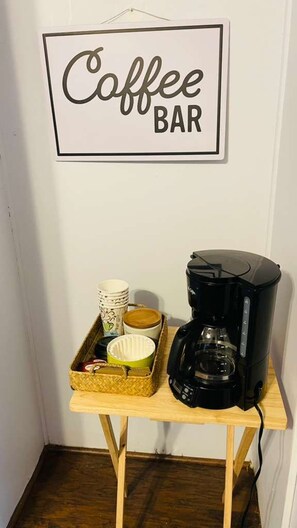 Un coin café aménagé avec une machine à café, des tasses et un plateau sur une table en bois, le tout placé contre un mur sur lequel est affiché un panneau indiquant « Coin café ».
