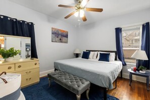 A bedroom with a bed, a dresser, a mirror, a ceiling fan, a window with curtains, and a painting on the wall. - Lakewood Park Main Floor, Free parking (Lakewood)