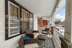 A covered porch with wicker furniture, a brick wall, and a view of a snowy street.