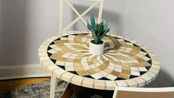 A round table with a mosaic top, two white chairs, a potted plant, and a painting on the wall.