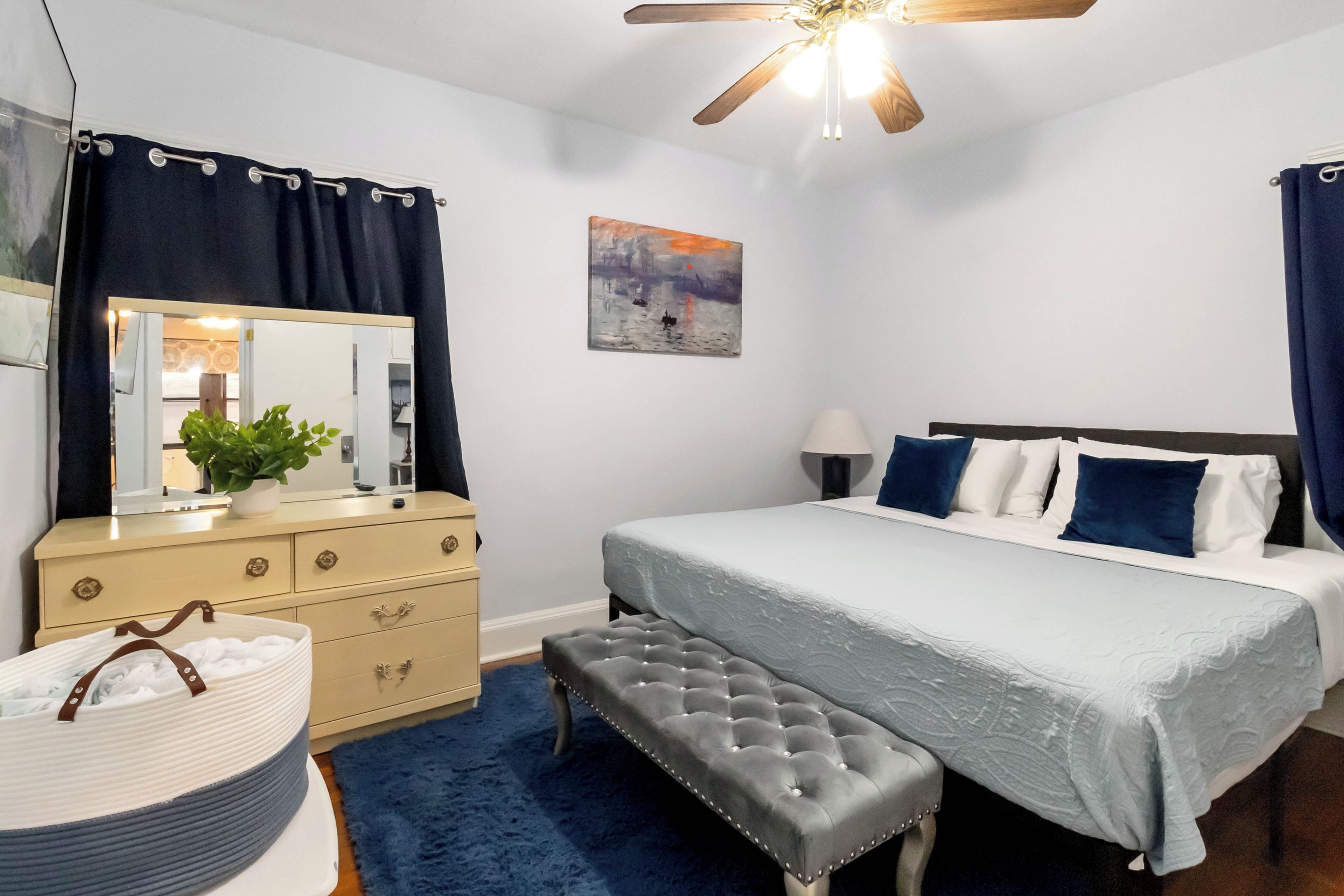 Ein Schlafzimmer mit Bett, Schminktisch, einer Bank, einem Deckenventilator und einem Bild an der Wand.