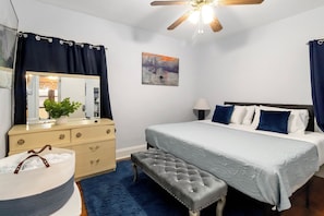A bedroom with a bed, a dresser, a bench, a ceiling fan, and a painting on the wall.