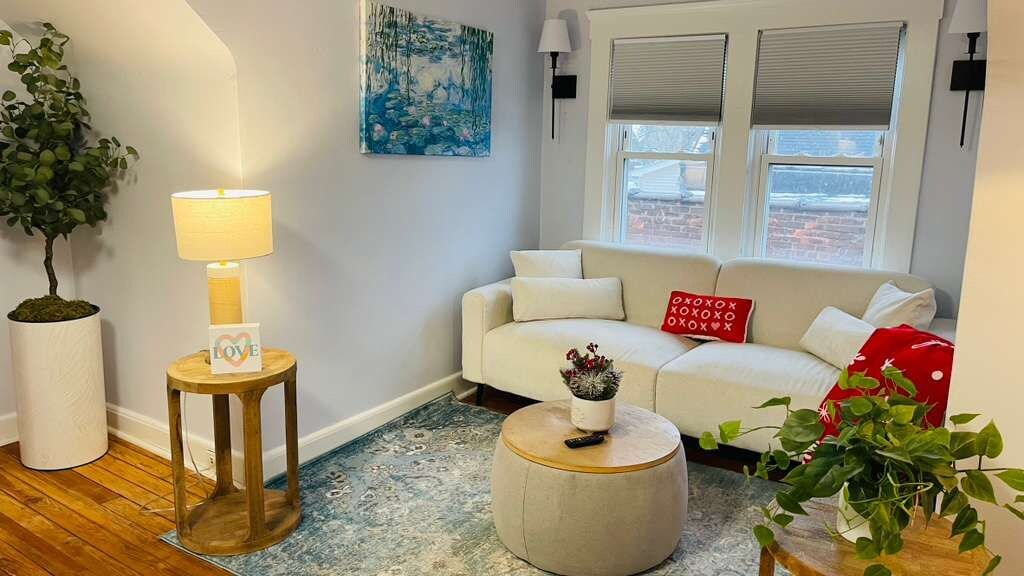 A living room with a sofa, a round coffee table, a lamp, a potted plant, and a painting on the wall.