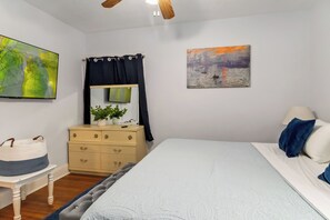 Een slaapkamer met een bed, een dressoir, een spiegel, een schilderij en een plant.