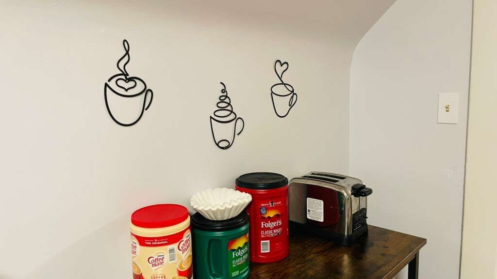 Una cocina con cafetera, tostadora y tres recipientes de café sobre una mesa de madera.