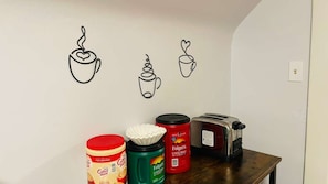A kitchen with a coffee maker, a toaster, and three coffee containers on a wooden table.