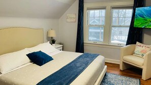 A bedroom with a bed, a chair, a TV, a window, and a wall decoration.
