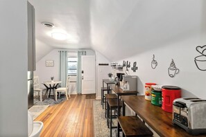 Une cuisine compacte avec un coin repas, un plancher en bois et une vue sur l’extérieur grâce à une porte ouverte.