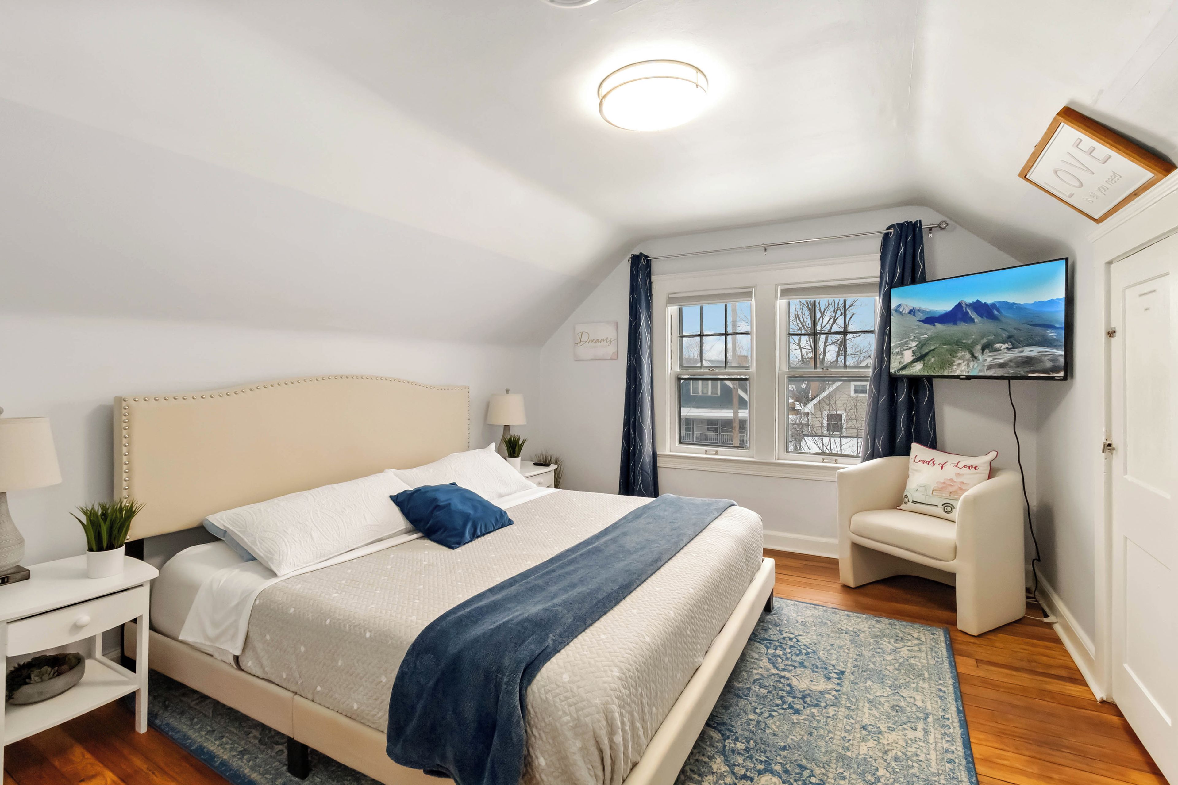 Ein Schlafzimmer mit Bett, Nachttischen, Fernseher, Sessel und Fenster mit Blick.