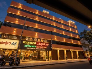 Un edificio de varios pisos con un restaurante llamado 'Kuttanad Restaurant', que muestra un cartel con imágenes de comida y texto en varios idiomas.