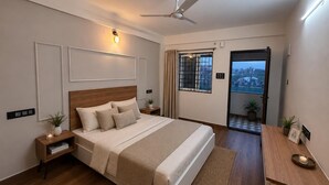 A modern bedroom with a large bed, bedside tables, a ceiling fan, and a view through an open door. - Petals Suites & Hotels (Bengaluru)