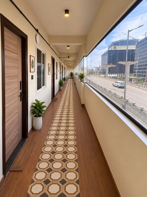 A hotel corridor with a patterned floor, potted plants, and a view of a construction site through large windows. - Petals Suites & Hotels (Bengaluru)