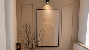 A hallway with a large vase of branches, a wall-mounted light, and a framed artwork. - Petals Suites & Hotels (Bengaluru)
