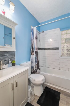 A bathroom with a white toilet, a sink with a soap dispenser, and a shower curtain. - ✨ Family-Friendly Charm in the Heart of Lakewood 🌿<br>Steps from Parks, Trails & Lake Views<br>Welcome to your serene escape in Lakewood—where convenience meets charm in one of Cleveland’s most walkable neighborhoods. (Lakewood)