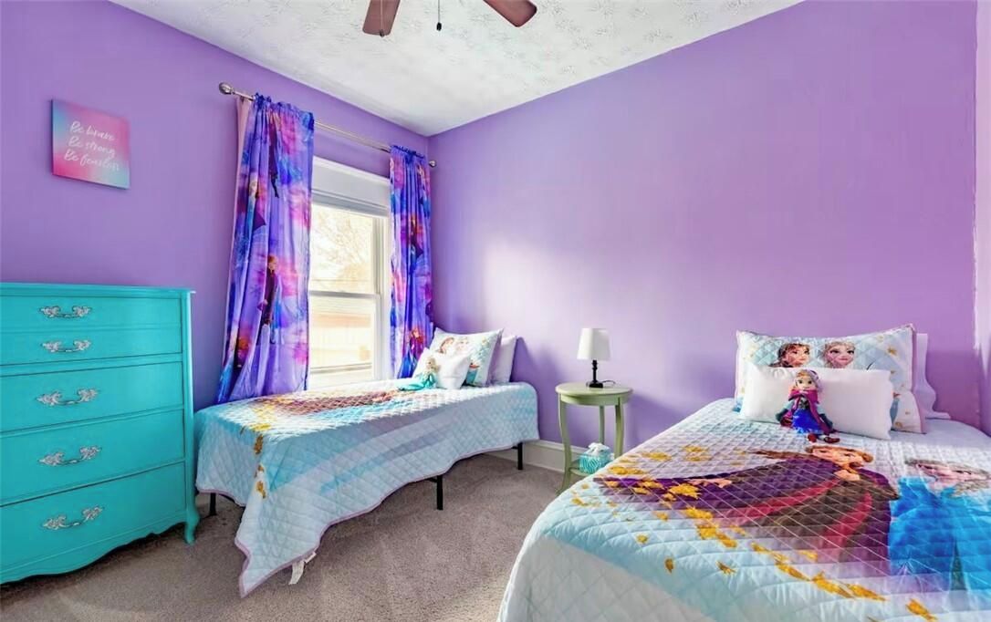 A bedroom with two beds, a dresser, a window with curtains, and a wall with a poster.