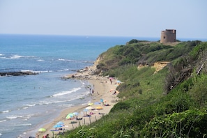A coastal beach with a tower on a cliff, sandy shore, and ocean waves.