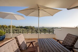 Una terraza con una mesa, sillas, dos sombrillas y vistas del paisaje.