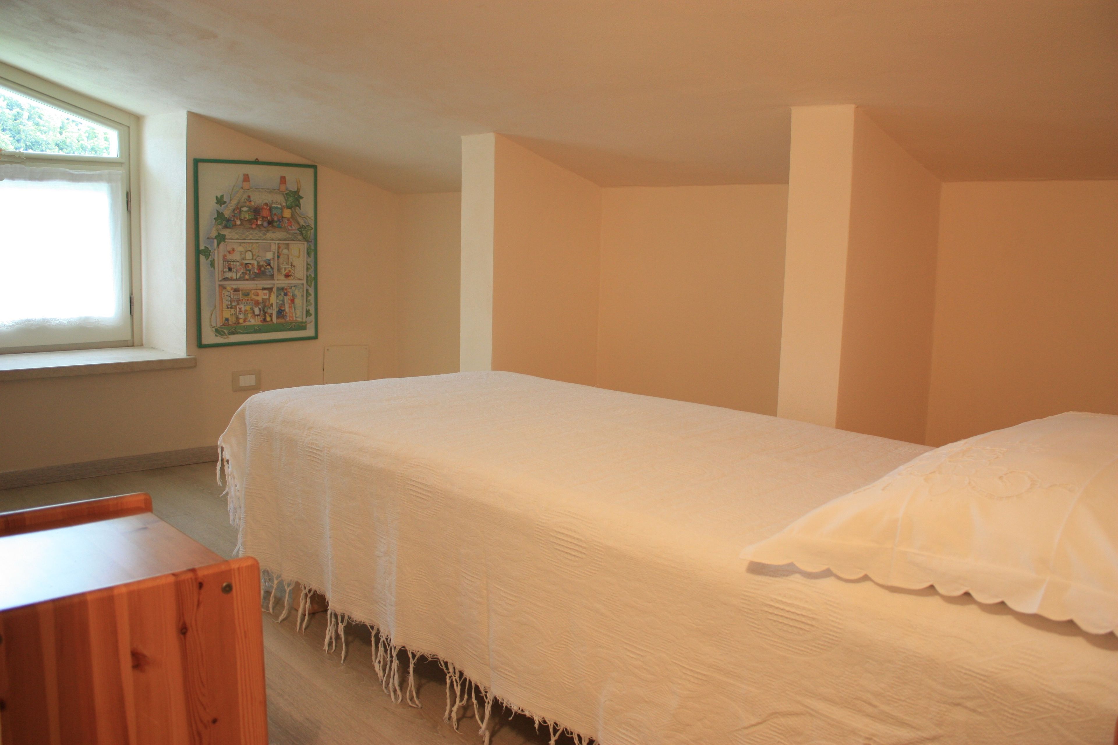 A bedroom with a single bed, a wooden bench, a window, and a wall-mounted picture.