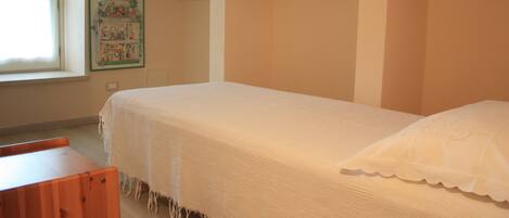 A bedroom with a single bed, a wooden bench, a window, and a wall-mounted picture.