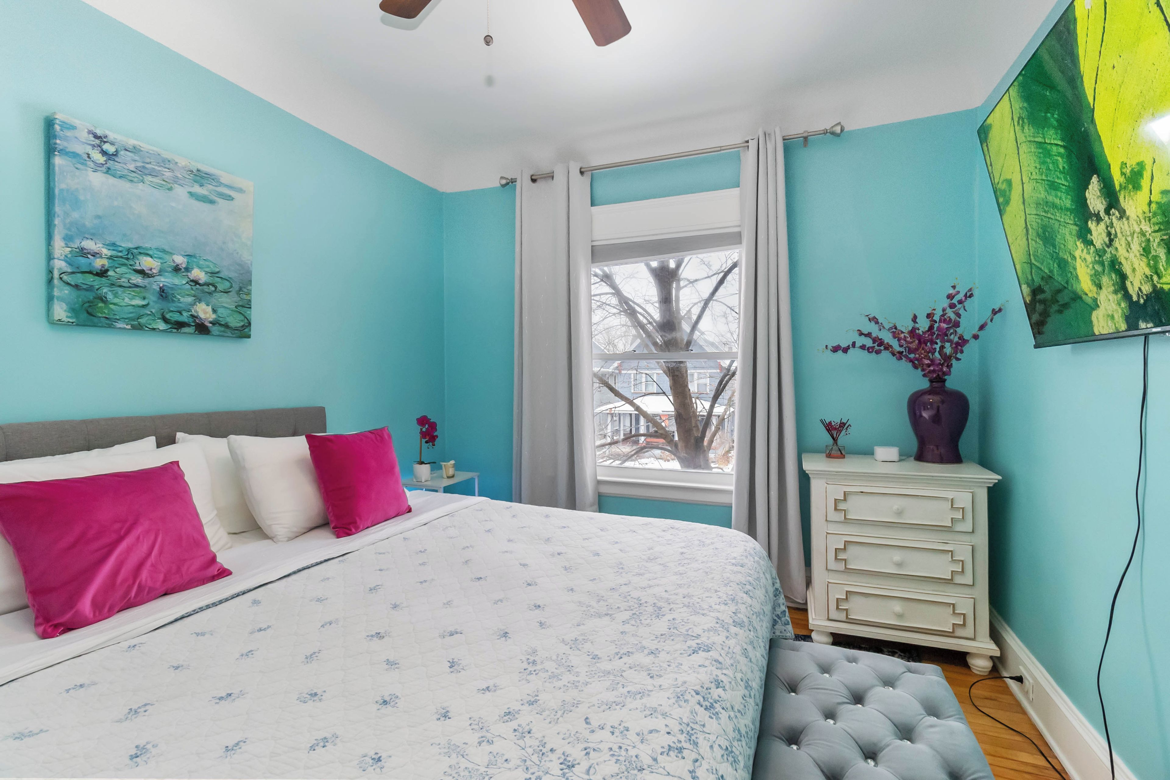 A bedroom with a bed, a dresser, a window, and two paintings.
