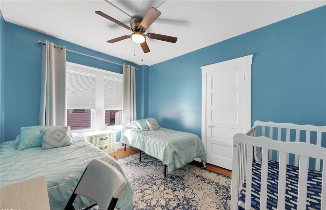 Une chambre avec deux lits, un ventilateur de plafond, une fenêtre avec des rideaux et un berceau.