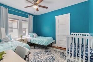 A bedroom with two beds, a crib, a ceiling fan, and a window with curtains. - ✨ Family-Friendly Charm in the Heart of Lakewood 🌿<br>Steps from Parks, Trails & Lake Views<br>Welcome to your serene escape in Lakewood—where convenience meets charm in one of Cleveland’s most walkable neighborhoods. (Lakewood)