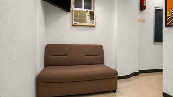Una habitación pequeña con un sofá marrón, una ventana con persianas, un extintor y una puerta.