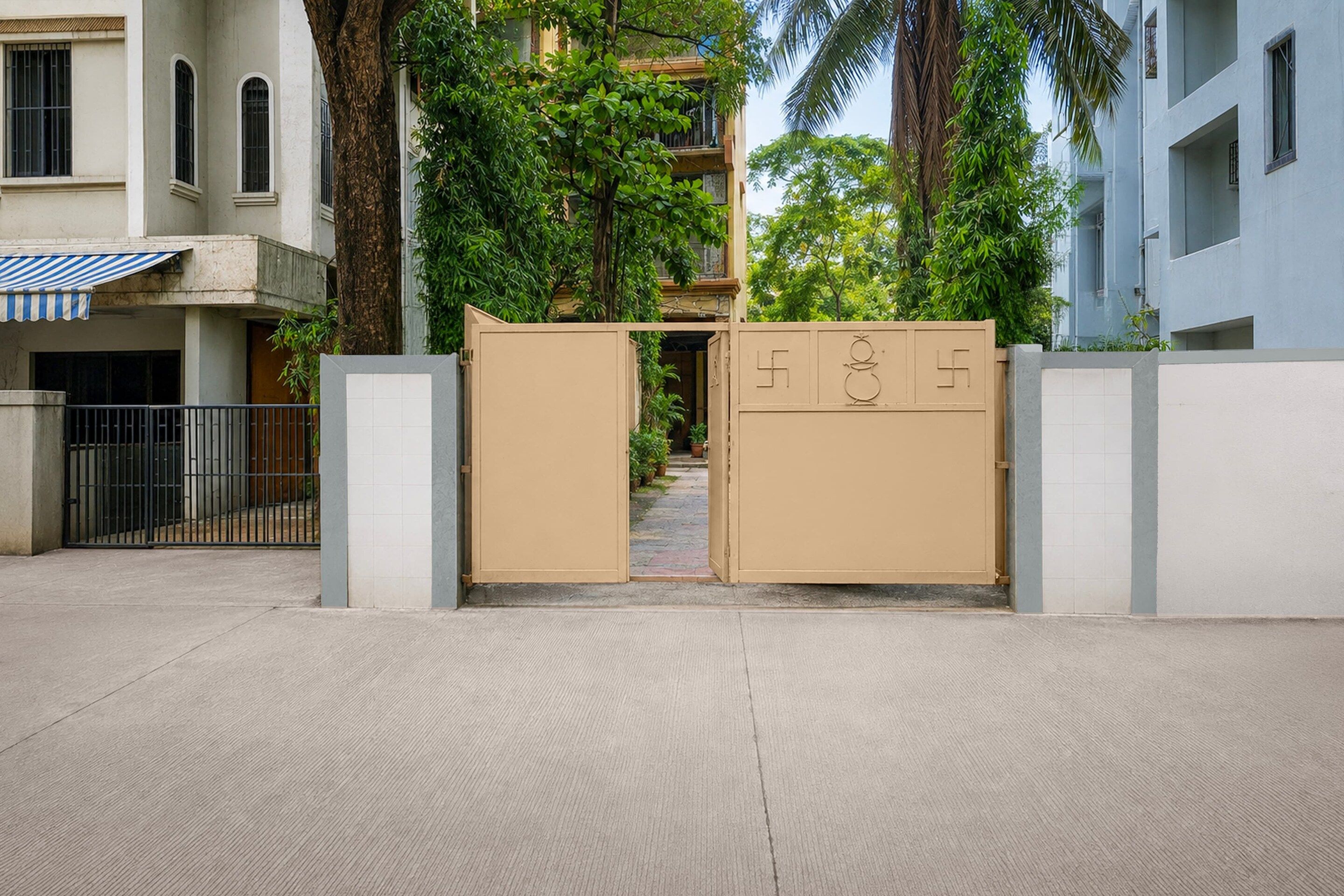 A gated entrance with a metal gate, a concrete pathway, and a building with a tiled facade and a blue awning.