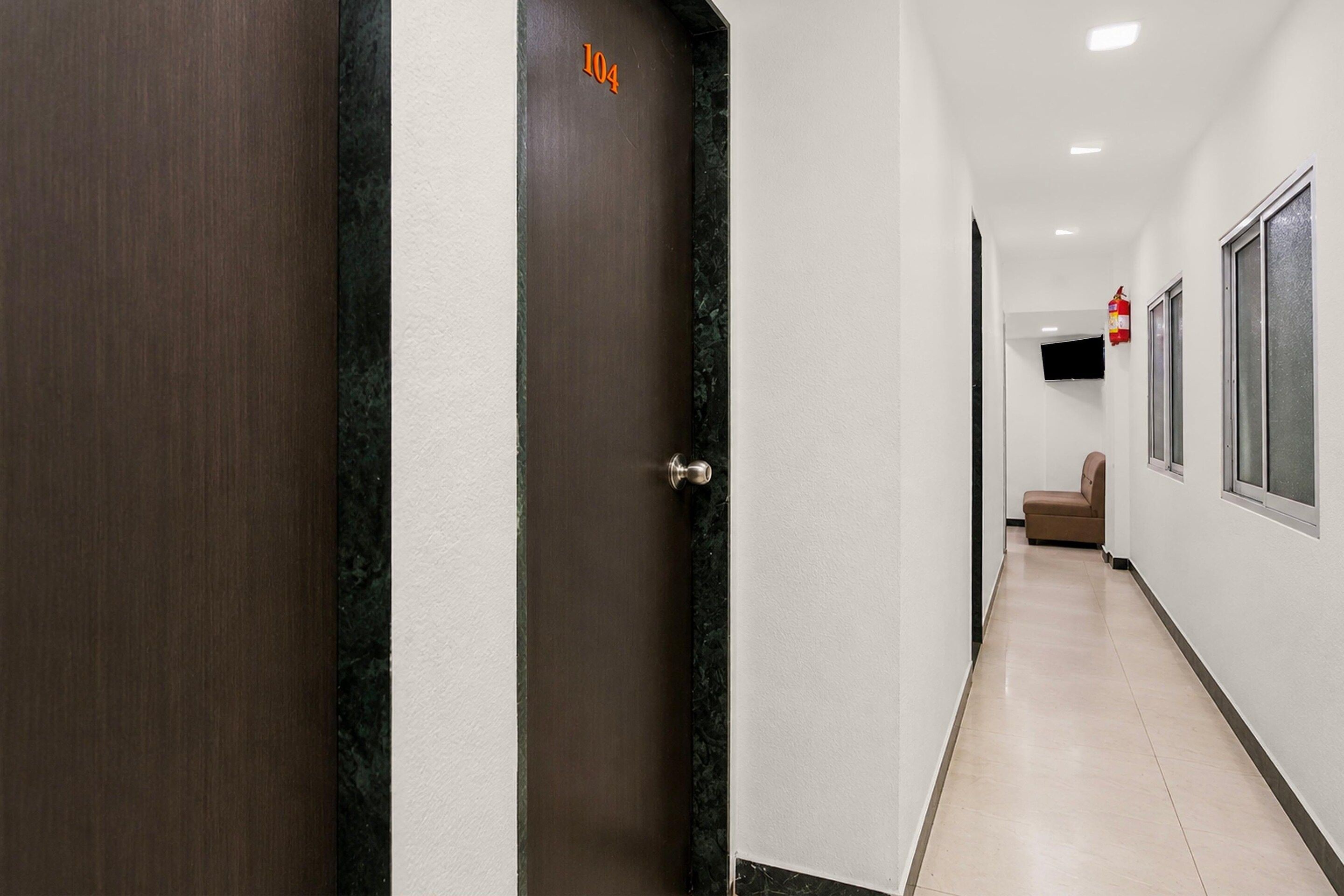 Un pasillo con una puerta marcada '104' que da a una habitación con una cama y un televisor.