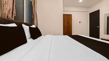 A hotel room with a bed, a wooden wardrobe, a door, and a window with curtains.