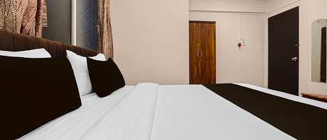A hotel room with a bed, a wooden wardrobe, a door, and a window with curtains.