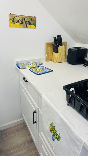 Eine Küche mit einem Holzschild mit der Aufschrift 'Grateful', einem Schneidebrett, Messern, einem Toaster und einem schwarzen Kunststoffbehälter.