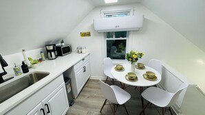Ett litet pentry med mikrovågsugn, kaffebryggare och diskho. Det finns en matplats med ett bord för två personer och en vas med blommor.