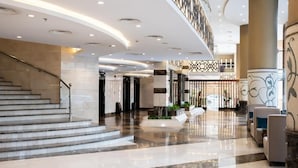 Um hall de hotel moderno com piso de mármore, escadaria, área de estar e painéis decorativos na parede.