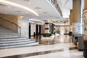 A modern hotel lobby with a marble floor, a staircase, seating area, and decorative wall panels. - Alaa Al Bayt Hotel (Makkah)