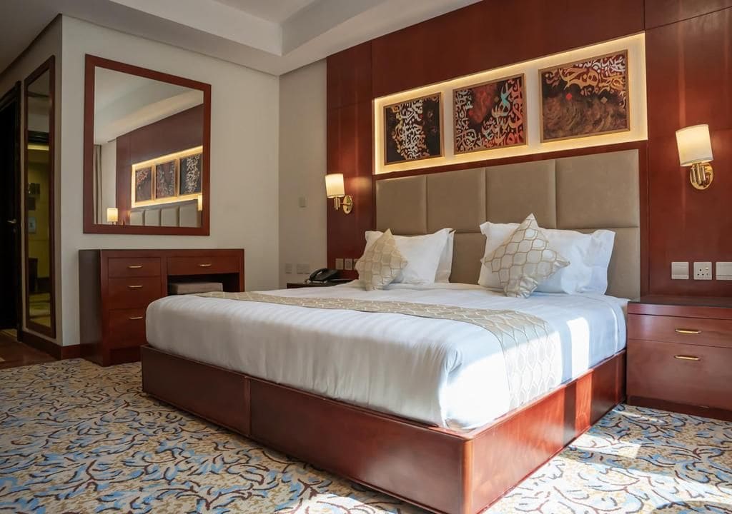 A hotel room with a large bed, a dresser, a mirror, and artwork on the wall.