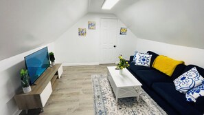 A modern living room with a flat-screen TV, a dark blue sofa with yellow cushions, a white coffee table, and a patterned rug. - CLE Tiny Hideaway- Free Parking (Cleveland)