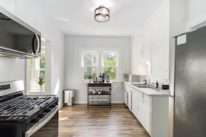 A modern kitchen with a gas stove, a refrigerator, and a window with a view of greenery. - Brand new Apartment in West Cleveland (Cleveland)