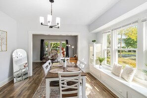 A dining area with a wooden table, white chairs, a chandelier, and a view of a garden through large windows. - Brand new Apartment in West Cleveland (Cleveland)