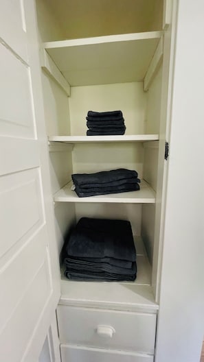 Ein weißer Kleiderschrank mit drei Einlegeböden und einer Schublade, gefüllt mit gefalteten schwarzen Handtüchern.